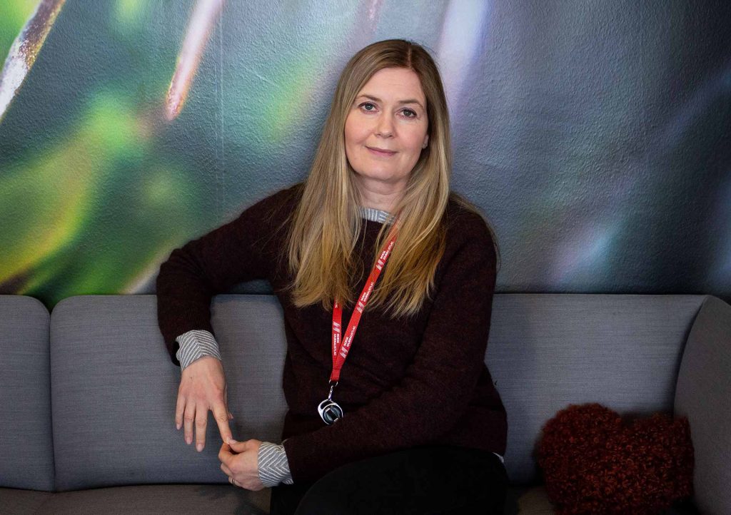 Hege Fagerheim, nestleder i Norsk Journalistlag, sitter foran en fargerik bakgrunn som er grønn og rosa