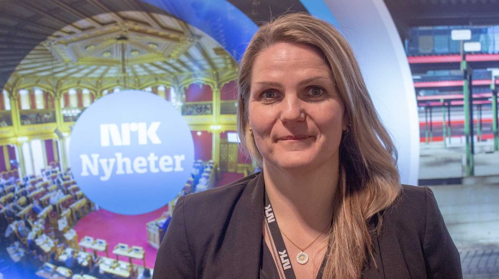 Karoline Riise Kristiansen er språksjef i NRK, hun står foran en skjerm med logoen NRK